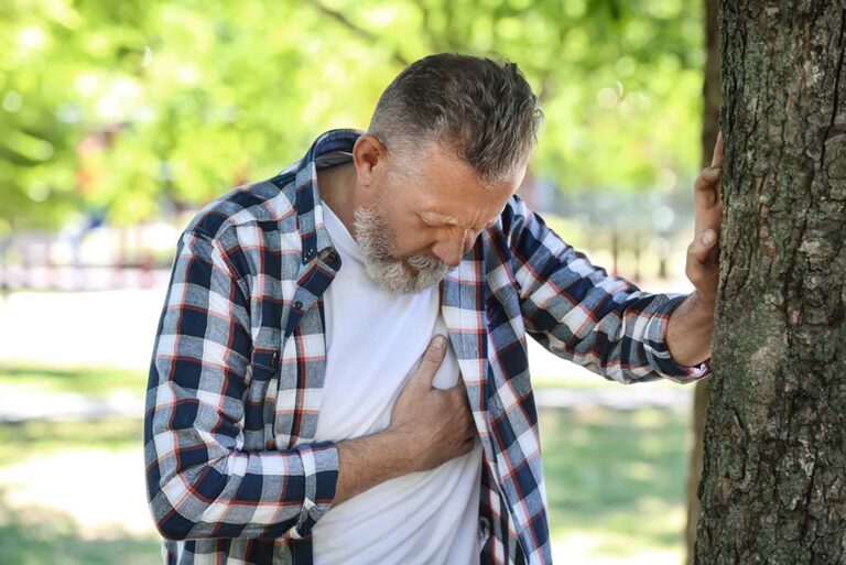 man with one hand on tree and other hand grabbing his chest