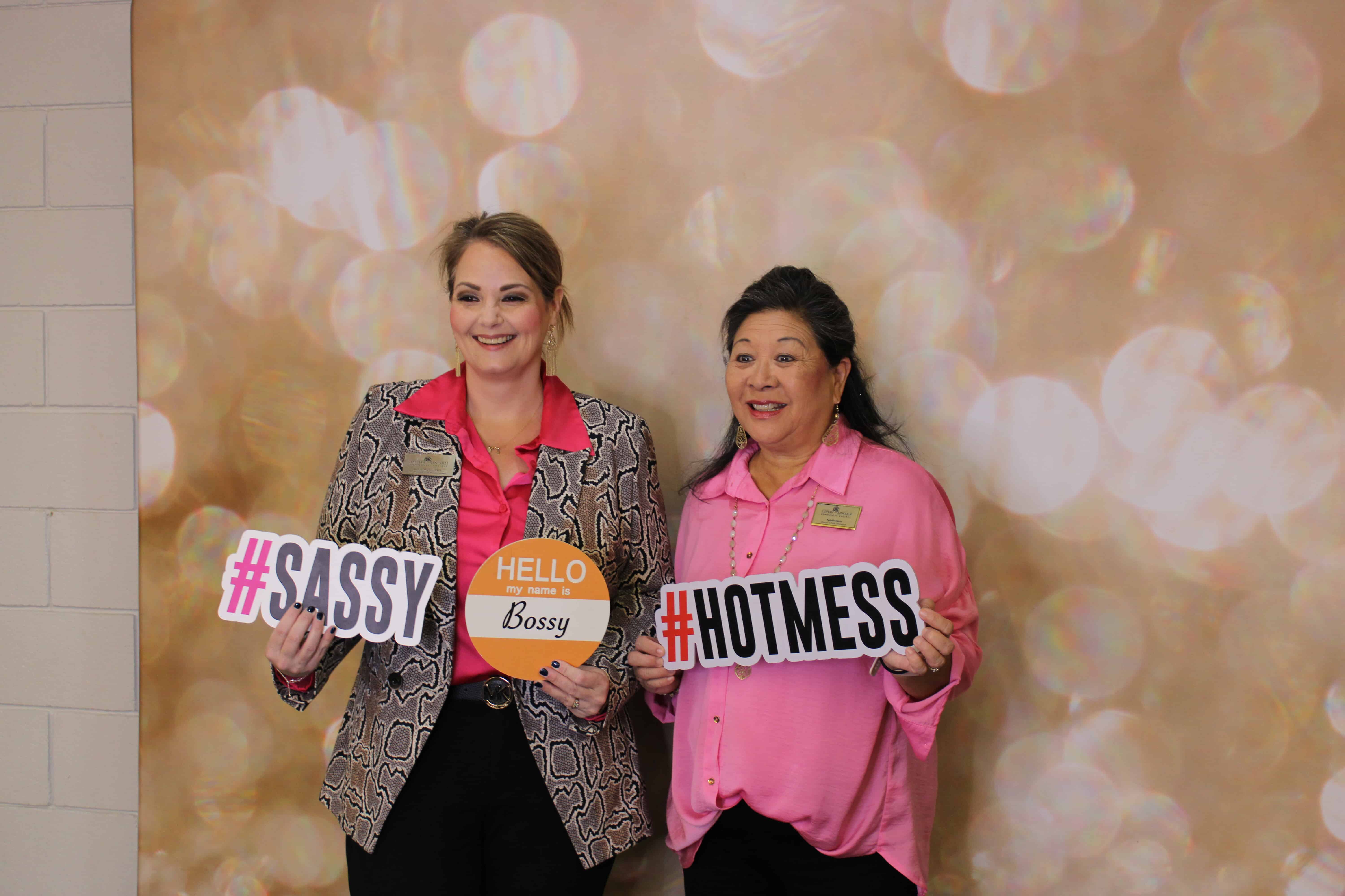 two women getting picture taken with cutouts reading sassy and hot mess